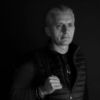 Black and white portrait of Michele Losito wearing a black crewneck shirt and quilted puffer vest with silver bracelets.