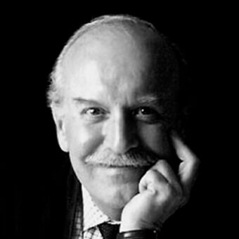 Black and white portrait of Sergio Asti, a man with gray hair, mustache, dark suit, and patterned tie, gazing forward pensively.