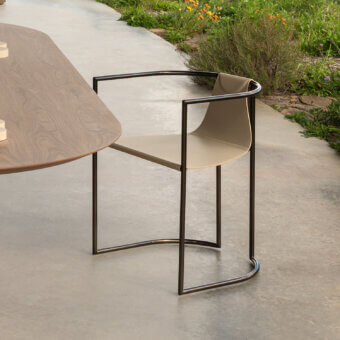 Jamiro chair, black metal frame, beige leather seat, beside round walnut table on gray concrete patio with plants.