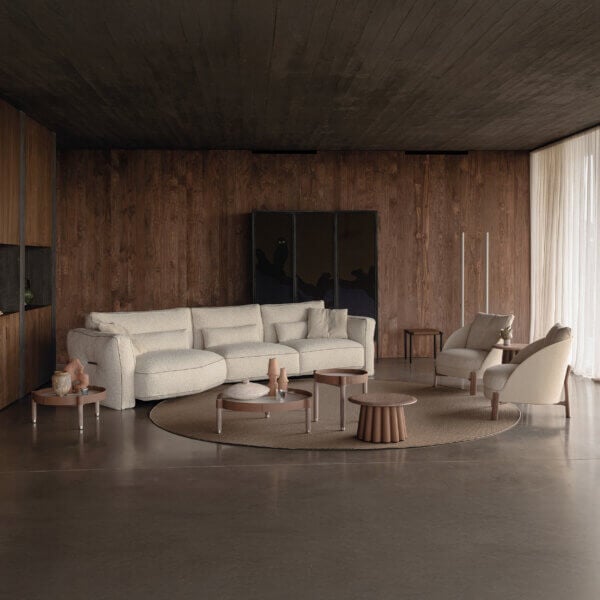 Modular sofa, off-white fabric, rounded shape, with jute rug, walnut paneling, and dark wood flooring in a minimalist living room setting.