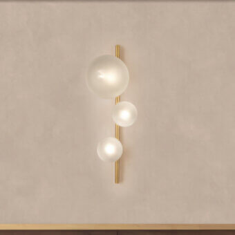Bubbles wall lamp, brushed gold metal, white glass globes, vertical arrangement, mounted on dark wood, textured beige wall.