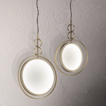 Gold suspension lamps, "Girasole" design, feature circular brass frames with opaque white globes, suspended from black cords against a gray textured wall.