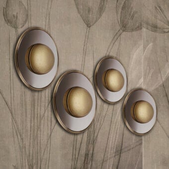 Cassoni Illusione wall lamps, brushed silver and gold, layered circular design against beige floral wallpaper.