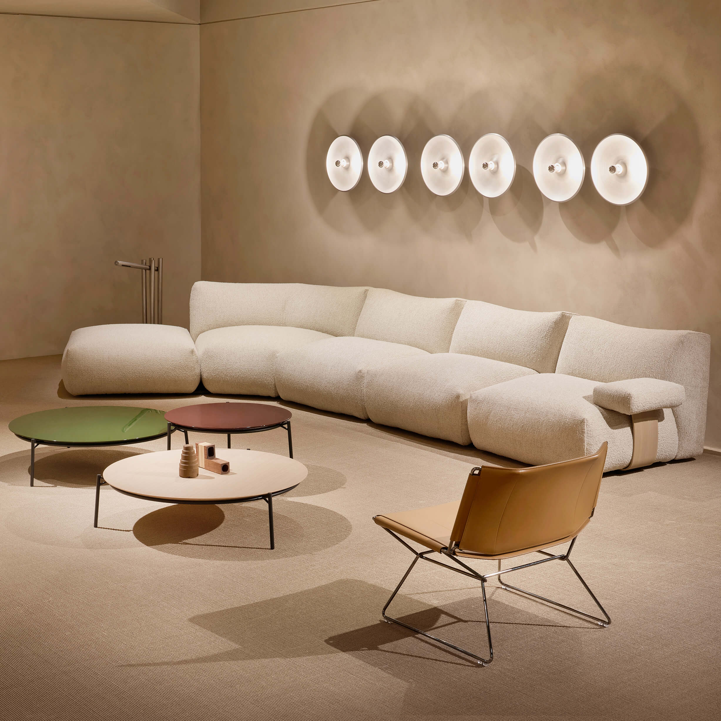 Modular sofa, off-white fabric, L-shape with three round coffee tables—black metal frames with green, burgundy, beige tops—and a tan leather chair.