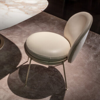 Sicis dining chair, cream leather upholstery, rounded silhouette with light green leather band, brushed metal legs, dark brown carpet.