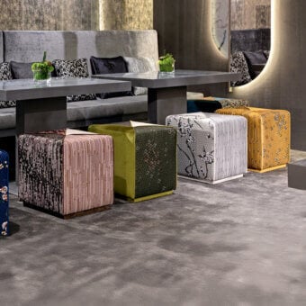 Sicis square ottomans with patterned upholstery arranged on gray carpet, featuring floral, striped, woven, and textured fabric designs.