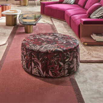 Sicis circus ottoman, red botanical print upholstery, circular form on reddish-brown and beige patterned rug in a modern living room.