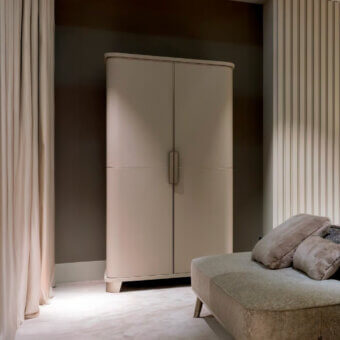 Sicis Don Giovanni cabinet, beige matte finish, curved top and vertical metal pulls, set against gray walls and beige curtains.