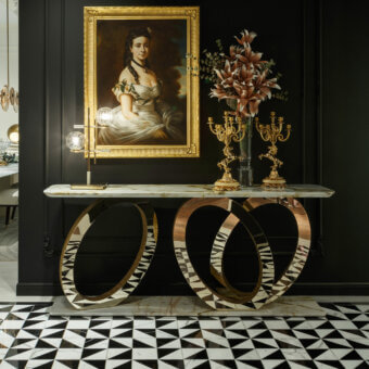 Marble console table, light green and gray veined top, with interlocking brushed gold metal ring base, against a dark gray paneled wall.