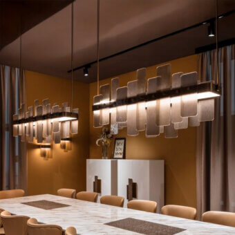 Sicis chandelier, metallic linear design, rectangular layered shades suspended over white console table in warm terracotta and mustard yellow room.