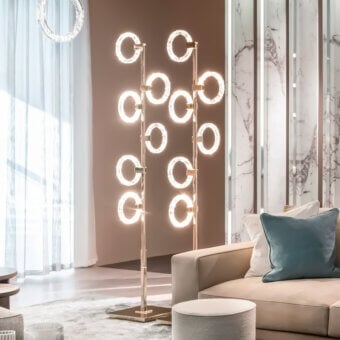 Brass floor lamp with circular illuminated elements and rectangular base in a modern interior setting with beige walls and marble accents.