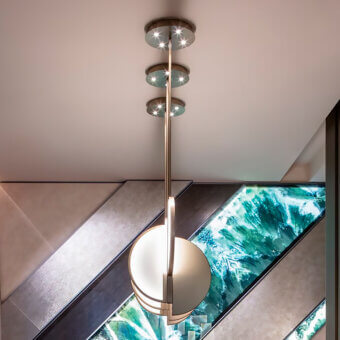 Sicis Venus suspension lamp, polished metal, half-sphere with tiered lights above a staircase featuring turquoise and silver glass artwork.