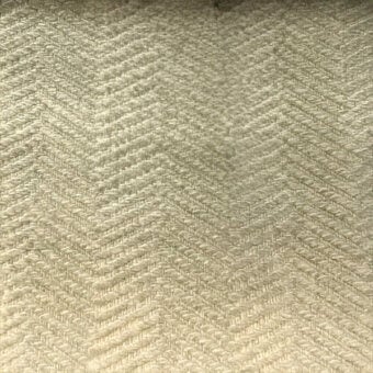 Herringbone fabric texture in muted beige, displaying a dense, diagonal weave with a matte finish and a small dark spot.