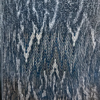 Woven textile with dark blue and light gray threads forming a dynamic, irregular pattern and slightly crinkled surface texture.