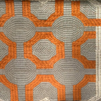 Geometric textile sample with gray and orange circular and hexagonal patterns on a beige background, featuring textured rope-like gray areas.