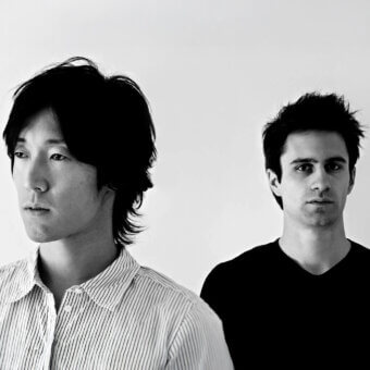 Two men portrait, fair skin, dark hair, striped shirt and black V-neck, white background, minimalist composition, even lighting, facial details.