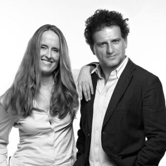 Black and white portrait of a woman in a light shirt and a man in a dark blazer, studio shot with neutral lighting.