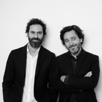 Black and white portrait of Edward Barber and Jay Osgerby, two men in dark suits against a white background, with crossed arms.