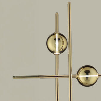 Mikado floor lamp, polished brass, geometric rods and spheres, bright white glow, neutral beige background, studio lighting.