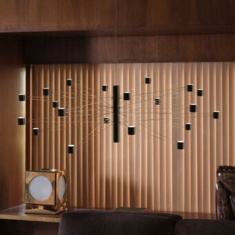 Kundalini Polar suspension lamp, black metal, radiating cylindrical shades, walnut wood slat wall, modern interior lighting.