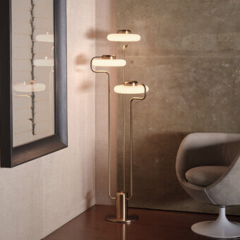 Kundalini Tratto floor lamp, brass finish, five oval shades on slender stem, modern interior with wood floor and textured wall.