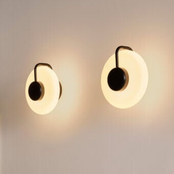 Kundalini Tratto wall lamps, white opaque shades, black metal arms, symmetrical pair on beige matte wall, diffused warm light.