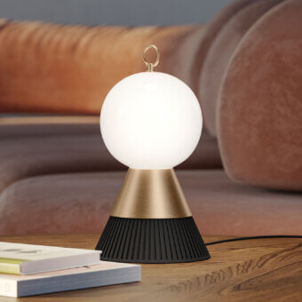 Masiero Bozu table lamp, brass and black, with spherical white shade on wood surface near leather sofa.