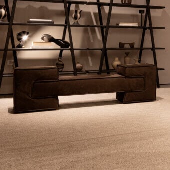 Verzelloni bench, brown textured fabric, rectangular form with integrated dark metal shelving displaying decorative objects.
