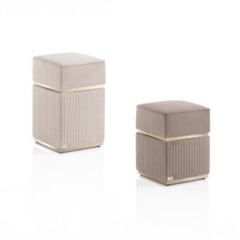Square velvet ottomans, light taupe finish, with gold metal band and ribbed rectangular base, displaying brand plaque detail.