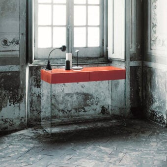 Red Glas Italia console table with rectangular drawers and curved stainless steel base against distressed gray plaster wall.
