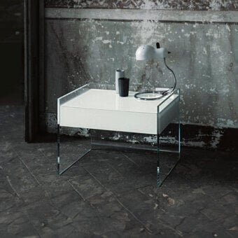 Glas Italia Cassoni Float nightstand, white surface, clear glass frame, on gray tile floor against textured concrete wall.