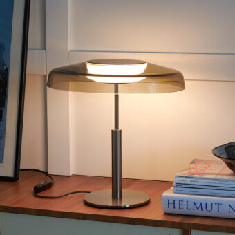 Dora table lamp, dark bronze and brushed metal, with a layered smoked gray and white acrylic lampshade on a wooden side table.