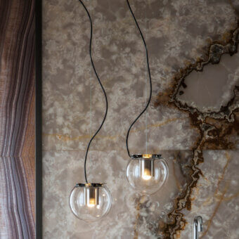 Globe suspension lamps with brushed brass frames illuminate brown & cream swirling patterned tiles, contrasted by dark wood paneling.