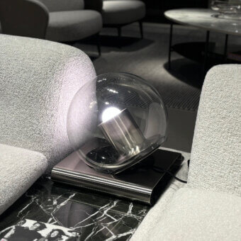 Globe table lamp, silver metal, spherical shade on black and white marble table with textured off-white armchairs, diffused warm light.