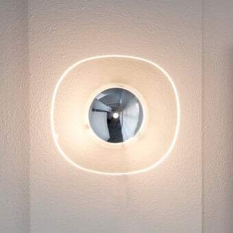Cassoni Oluce Yolk Wall Lamp, mirrored disc, warm white light, beige textured wall, minimalist circular design.