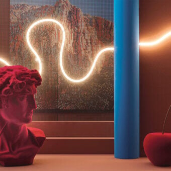 Still life with red David bust, blue column, and cherry, lit by neon against terracotta wall and grid window backdrop.
