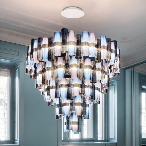 Chandelier, iridescent fabric, tiered cylindrical shades cascade from a white ceiling mount in a room with pale blue walls and green window frames.
