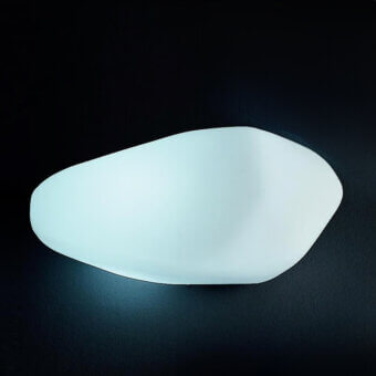 Wall light, white polyethylene, organic asymmetrical shape emitting diffused blue-white light against a dark gray backdrop.