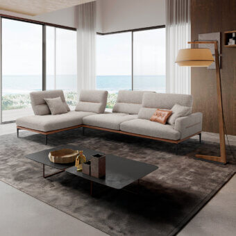 Modular sofa, light gray fabric, leather pillows, with wood floor lamp, black coffee table, and ocean view backdrop.