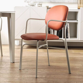 Terracotta armchair with rounded backrest and square seat, brushed silver metal frame, set against white kitchen and wood flooring.