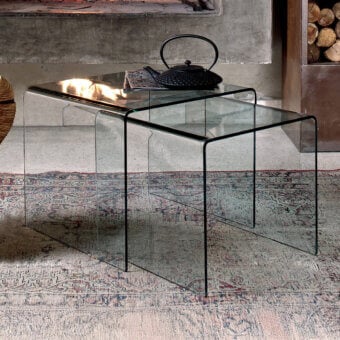 Bontempi Igloo side tables with black metal frames and clear glass tops nested on a patterned rug before a lit fireplace.