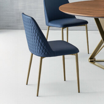 Bontempi Margot chair, deep blue quilted leather, high back with curved wings and brushed gold tapered legs, studio setting.