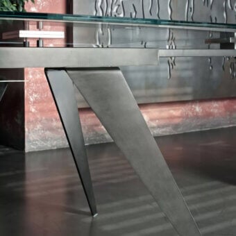 Extendable table, glass and brushed grey metal, with angular converging legs and a rectangular tabletop featuring a linear metallic accent.