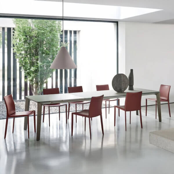 Dining table with light gray stone top, six red metal chairs, and gray conical pendant lamp in minimalist room setting.