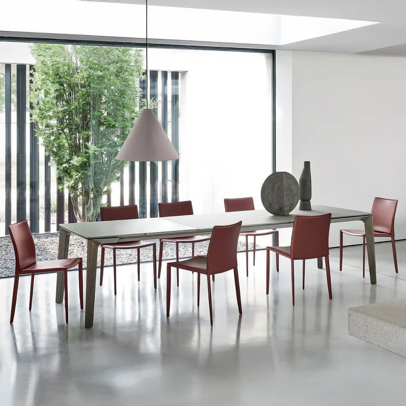 Dining table with light gray stone top, six red metal chairs, and gray conical pendant lamp in minimalist room setting.