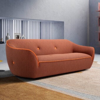 Terracotta Cassoni bebop sofa with rounded shape and orange trim, set in a minimalist room with gray wall and patterned rug.