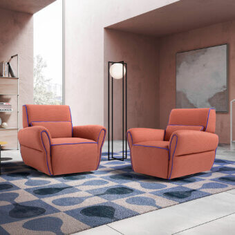 Coral lounge chairs with blue trim sit on a blue rug in a pink room with a white floor lamp and Bauhaus book.