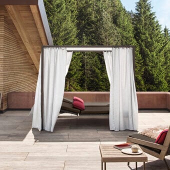 Superior Ethimo Allaperto daybed with dark gray metal frame, matte teak platform and flowing white curtains for outdoor relaxation