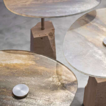 Superior Arte Veneziana Rascino side table with extra-clear baked glass displaying swirling amber, gold, and beige tones, built with a textured travertine base and satin steel