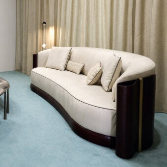 Luxury Bellotti Ezio 2026‑01 sofa upholstered in off‑white Tecnabuk textile with dark brown hide‑covered base and wing panels accented by satin‑gold metallic strip, crescent shape and curved lines